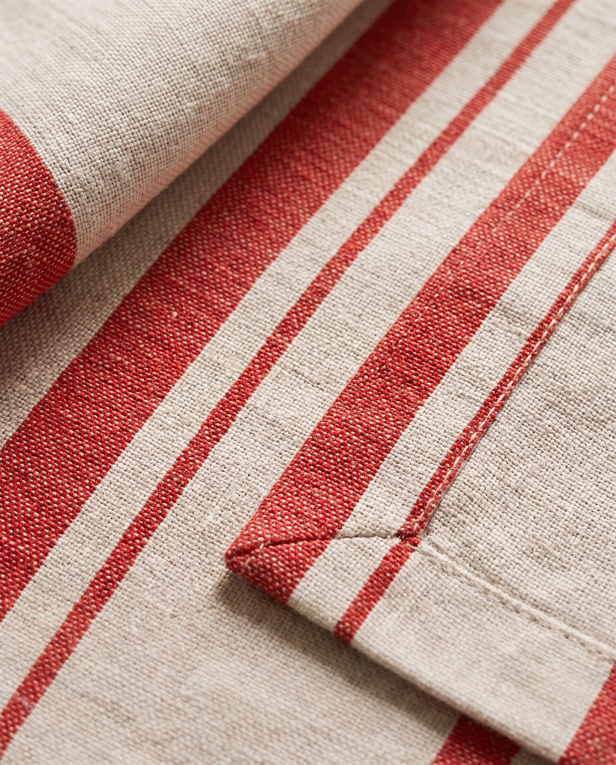 Close-up of the woven red stripe, the double-folded hem and the mitred corner of a Righe napkin